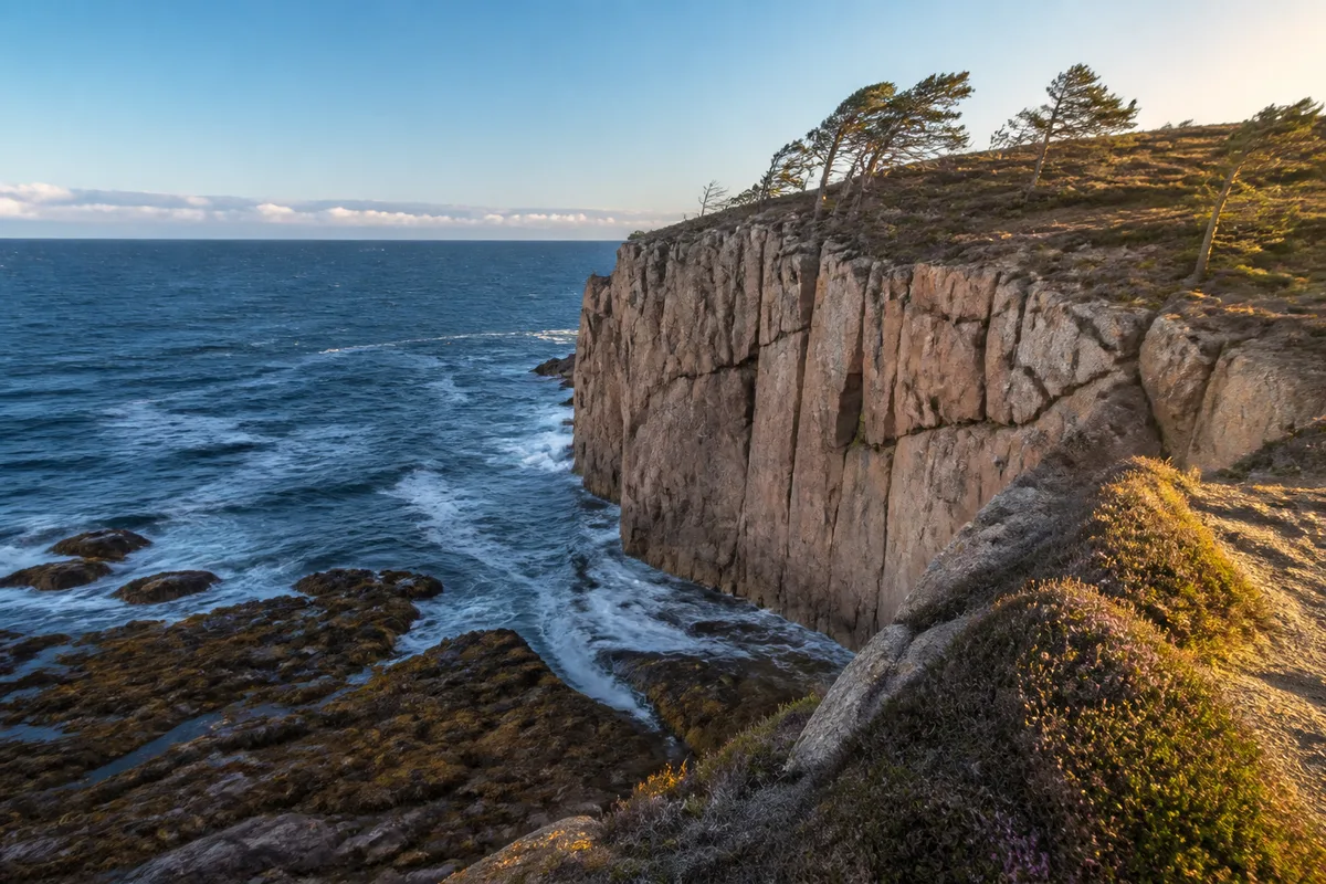 Falaise de granite rose plongeant dans l’océan sous un ciel de fin de journée
